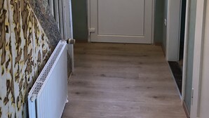 En hall med en vit dörr, ett element och en trappa med ett träräcke.