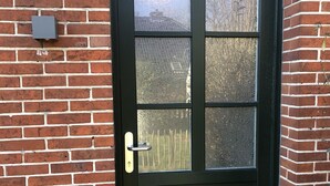 En svart dörr med en glasruta, ett metallhandtag och ett litet trappsteg som leder upp till ingången.