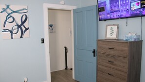Une pièce avec une porte bleue, une commode en bois et un téléviseur fixé au mur qui diffuse des images d’un paysage urbain.