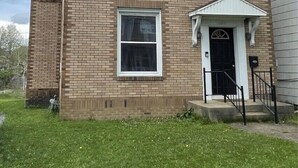 Une maison à deux étages, construite en briques, avec un porche à l’avant, une porte d’entrée noire et un petit garage attenant.