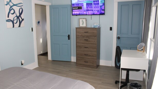 Une chambre à coucher avec un lit, une commode, un bureau, un téléviseur et une porte.