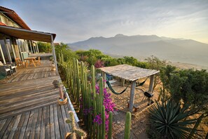 Una terraza de madera con mobiliario exterior, una hamaca y una pérgola con vistas a las montañas.