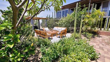 Eine Terrasse mit Holztisch und Stühlen, umgeben von üppiger Vegetation und Kakteen.