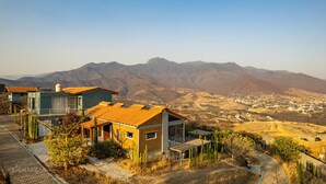 Una casa moderna con techo amarillo, rodeada de vegetación desértica y montañas al fondo.