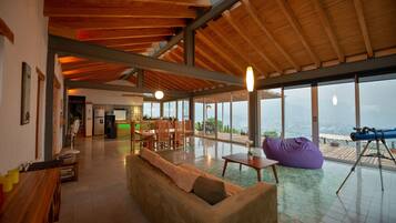 Un'ampia zona giorno con soffitto in legno, un divano, un pouf, un telescopio e vista sull'esterno.