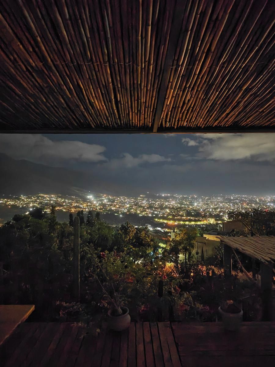 Vista desde un espacio exterior cubierto con piso de madera, que da al paisaje urbano de noche.