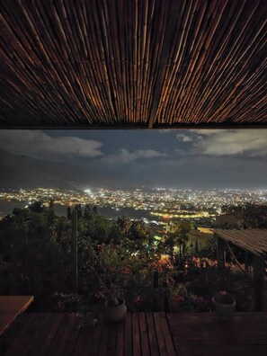 Uitzicht vanuit een overdekt terras met houten vloer, op een stadsbeeld in de nacht.