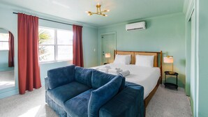 Une chambre d’hôtel avec un lit, un canapé bleu, un lustre et une fenêtre avec des rideaux.