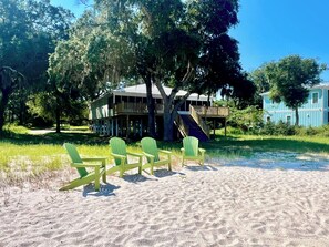 A beachfront property with a wooden deck, outdoor seating, and a large tree.