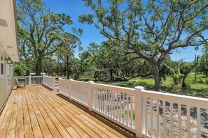 A wooden deck with white railings, surrounded by trees and a clear sky.