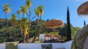 Una terraza con mobiliario exterior, palmeras y vistas a un paisaje montañoso.