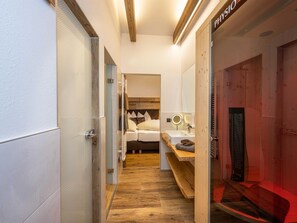 A narrow hallway leading to a bedroom with a bed, a bedside table, and a mirror. - Apartment "S'HOAMELIGE" - House Wiederkehr (Schladming)