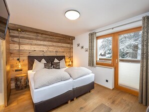 A bedroom with a wooden headboard, a double bed with checkered bedding, two bedside lamps, a nightstand, and a window with curtains. - Apartment "S'HOAMELIGE" - House Wiederkehr (Schladming)
