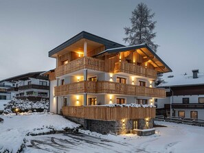 A multi-story chalet with wooden balconies, stone foundation, and snow-covered surroundings. - Apartment "S'HOAMELIGE" - House Wiederkehr (Schladming)