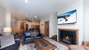 A living room with a fireplace, a sofa, a coffee table, and a television displaying a ski scene.