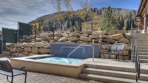 A pool area with a stone wall, a pool with a blue tiled edge, and a bench.