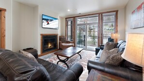 A living room with leather sofas, a fireplace, a television, and a balcony with a view of the outside.