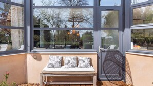 A sunlit room with a wooden bench and cushions, large windows, and a woven light fixture.
