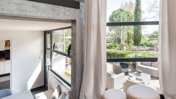 A modern room with a large window, a view of an outdoor garden, and a dining area visible through the window.