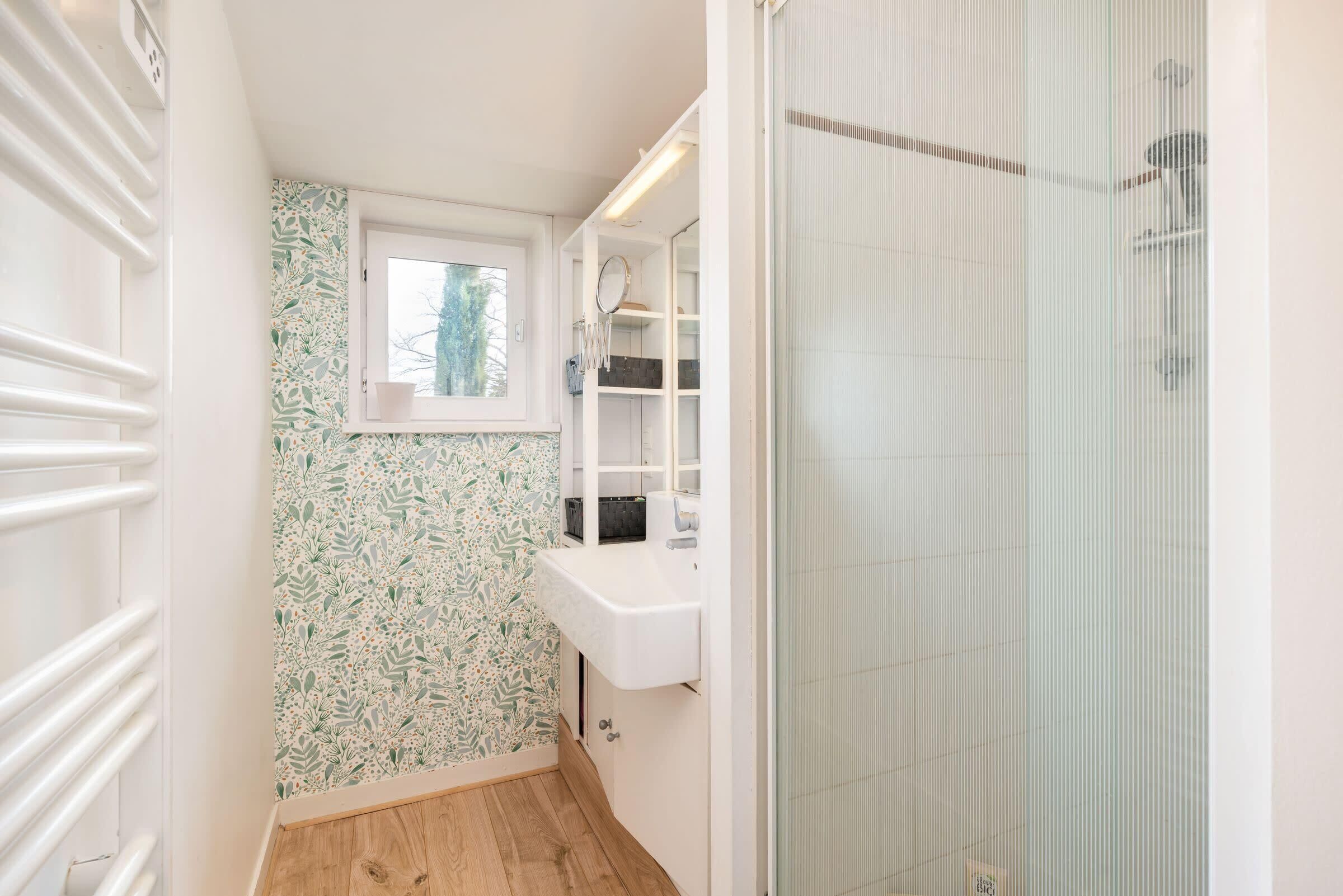 A narrow bathroom with a window, a sink, and a shower area.