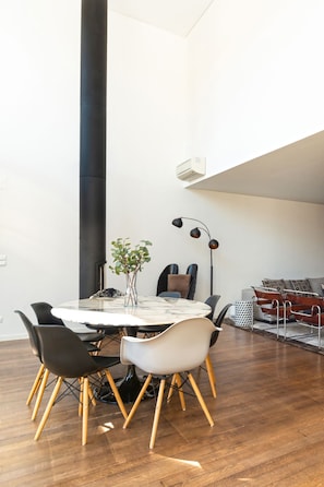 Een moderne eetruimte met een ronde tafel, zwart-witte stoelen, een vaas met groene planten en een hoge zwarte kolom.