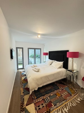 Een moderne slaapkamer met een groot bed, twee bedlampen, een kamerbreed tapijt en uitzicht door de glazen deuren.