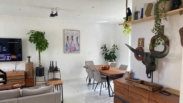 Ein modernes Wohnzimmer mit einer Couch, einem Fernseher, einem Esstisch, Stühlen und einer Holzkommode.