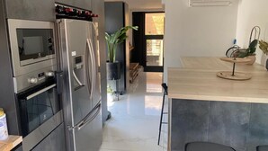 Eine moderne Küche mit Einbauofen, Mikrowelle und einem Edelstahl-Kühlschrank. Eine kleine Kochinsel mit Spüle und Barhocker ist ebenfalls vorhanden.