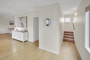 Une pièce spacieuse avec un plancher en bois, une console blanche, un tableau et un escalier menant à un autre niveau.