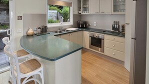 Une cuisine moderne dotée d’un îlot central, d’appareils électroménagers en acier inoxydable et offrant une vue sur le jardin.