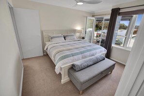 Une chambre à coucher avec un lit, une fenêtre donnant sur un beau paysage, une porte et un ventilateur de plafond.