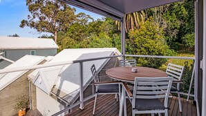 Un balcon avec une table et des chaises en bois, donnant sur un quartier résidentiel avec des maisons et des arbres.