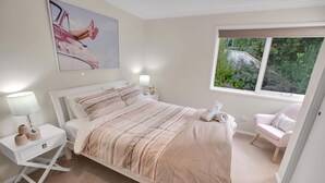 A bedroom with a bed, bedside tables, a chair, a window with a view, and a painting on the wall.