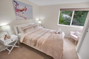 A bedroom with a bed, bedside tables, a chair, a window with a view, and a painting on the wall.