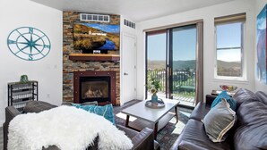 A living room with a fireplace, a large window, and a view of the outdoors.