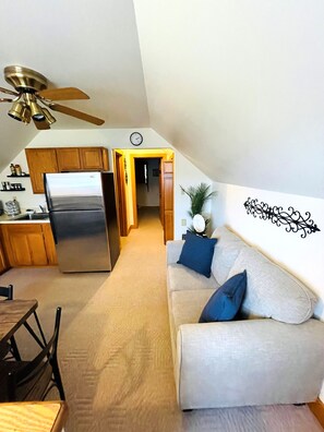 A compact living space with a kitchenette, a ceiling fan, a sofa with cushions, and a decorative wall piece.