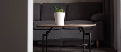 Ein runder Holztisch mit einem weißen Pflanzgefäß darauf, vor einer grauen Couch platziert.