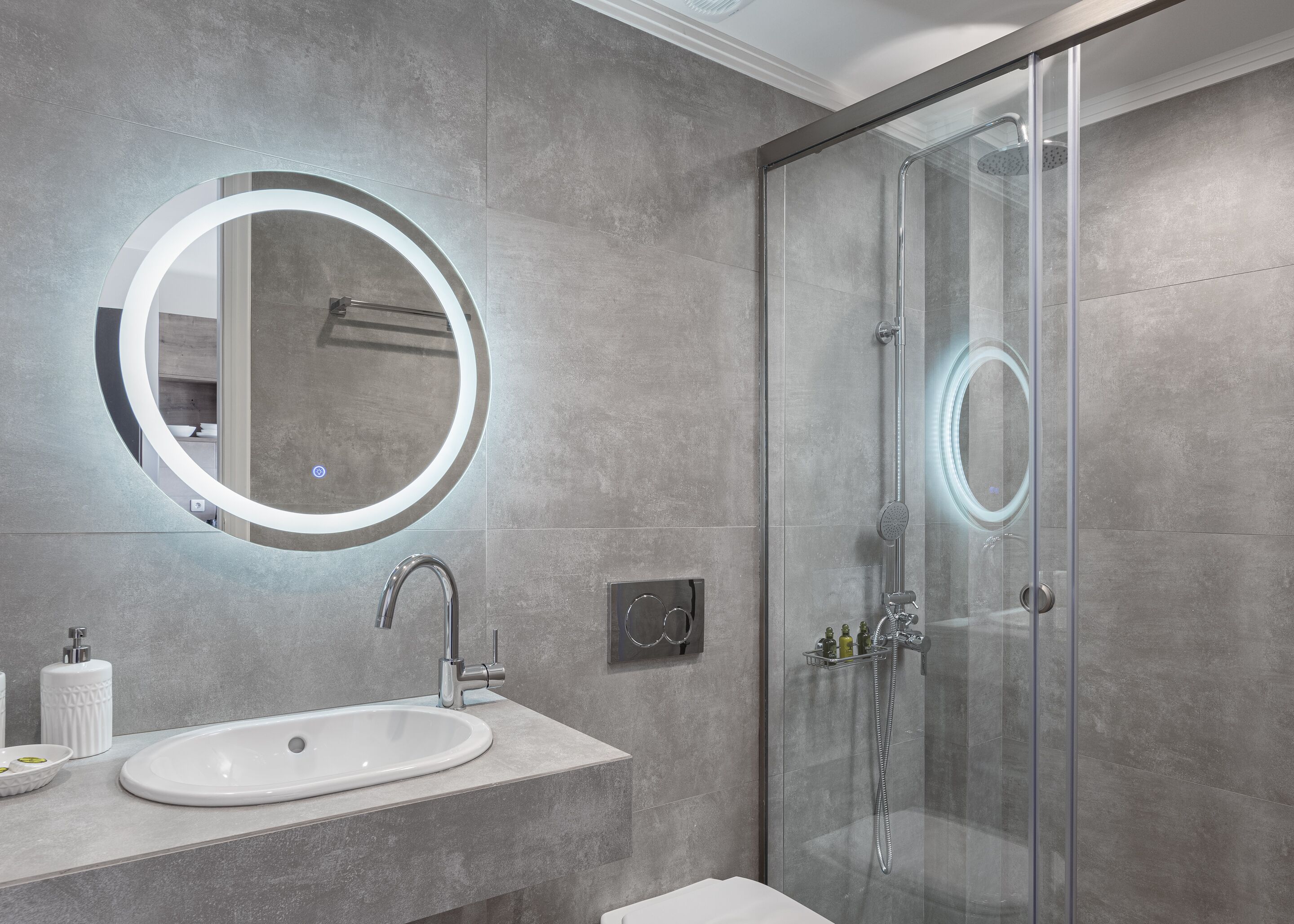 A modern bathroom with a round mirror, a sink, and a glass-enclosed shower.