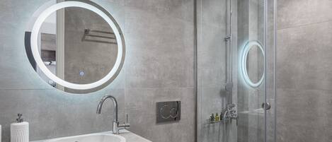 A modern bathroom with a round mirror, a sink, and a glass-enclosed shower.