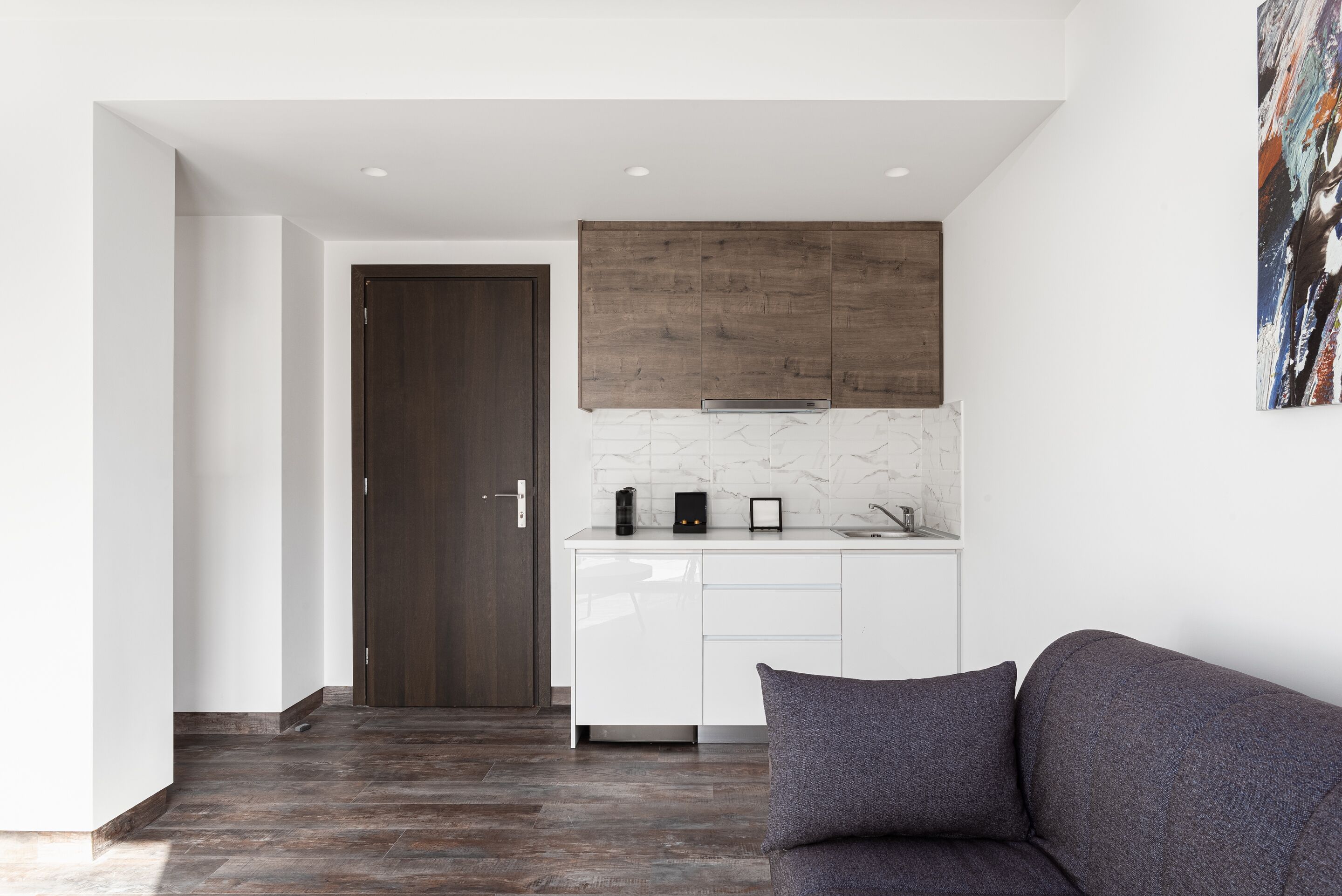 A modern kitchen with white cabinets, a dark wooden door, and a marble backsplash.