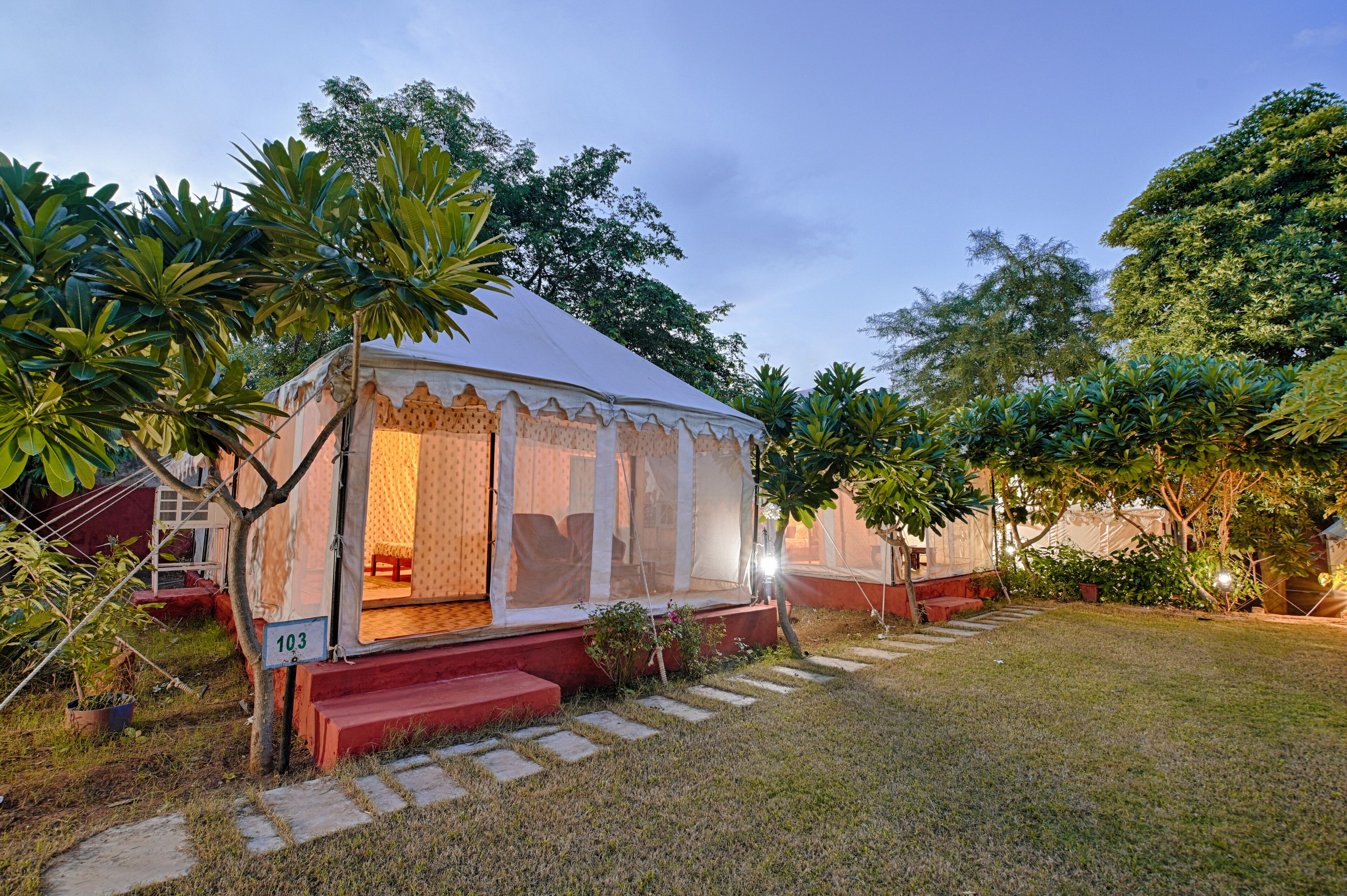 A tented accommodation with a covered outdoor seating area, surrounded by lush greenery.