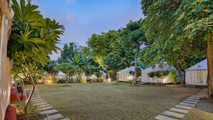 A well-maintained garden with a grassy lawn, stone pathway, and several trees. - Ranthambore Tiger Resort by Park Tree (Sawai Madhopur)