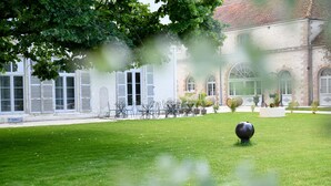 A courtyard with a lawn, outdoor seating, and a building with windows and shutters. - Maison Qualisterra - Chambre d'Hôtes (Bar-sur-Aube)