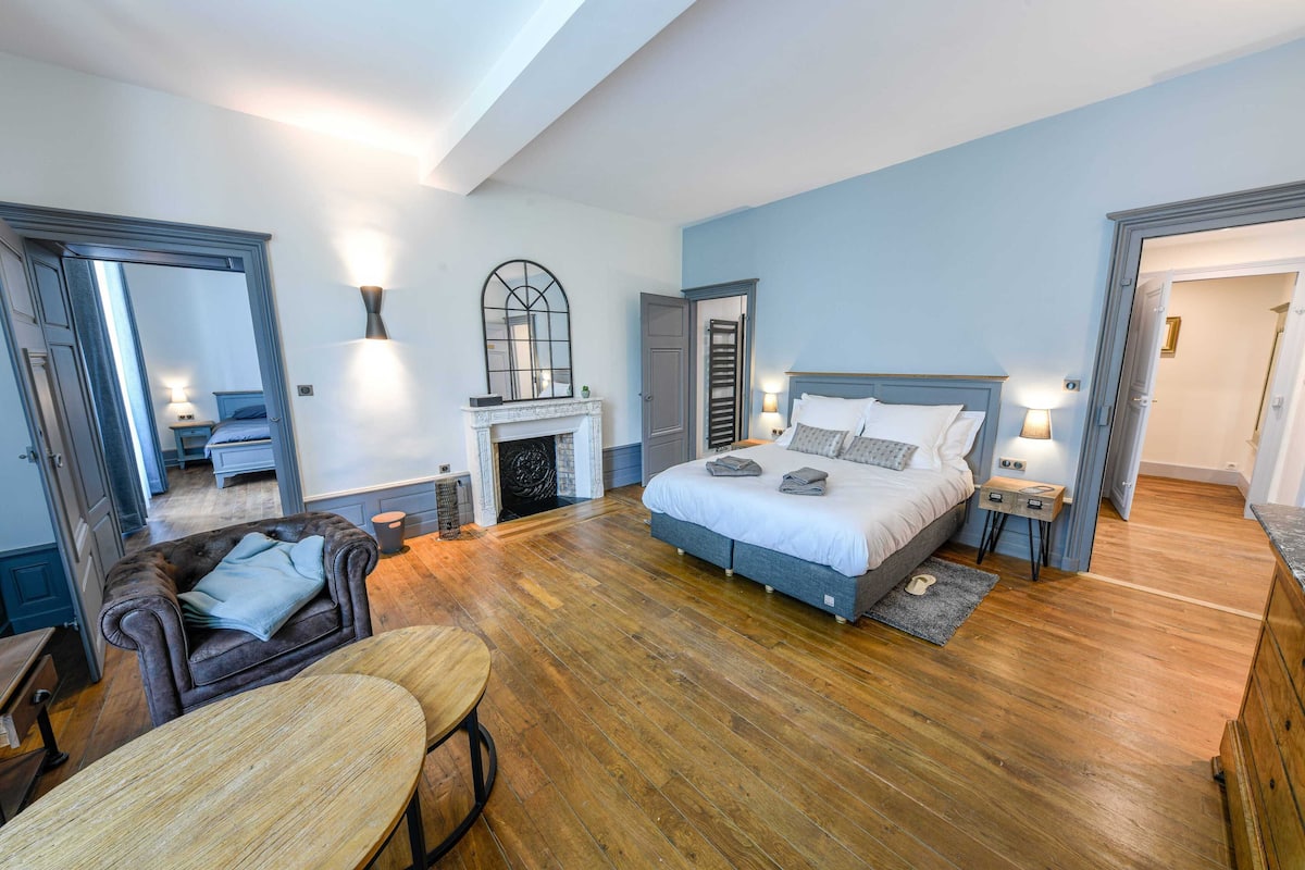 Une chambre avec un grand lit, une cheminée, un miroir et un plancher en bois.