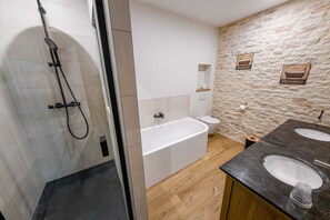 Een moderne badkamer met een douchecabine van glas, een vrijstaand bad, een toilet en een wastafel met twee kommen.