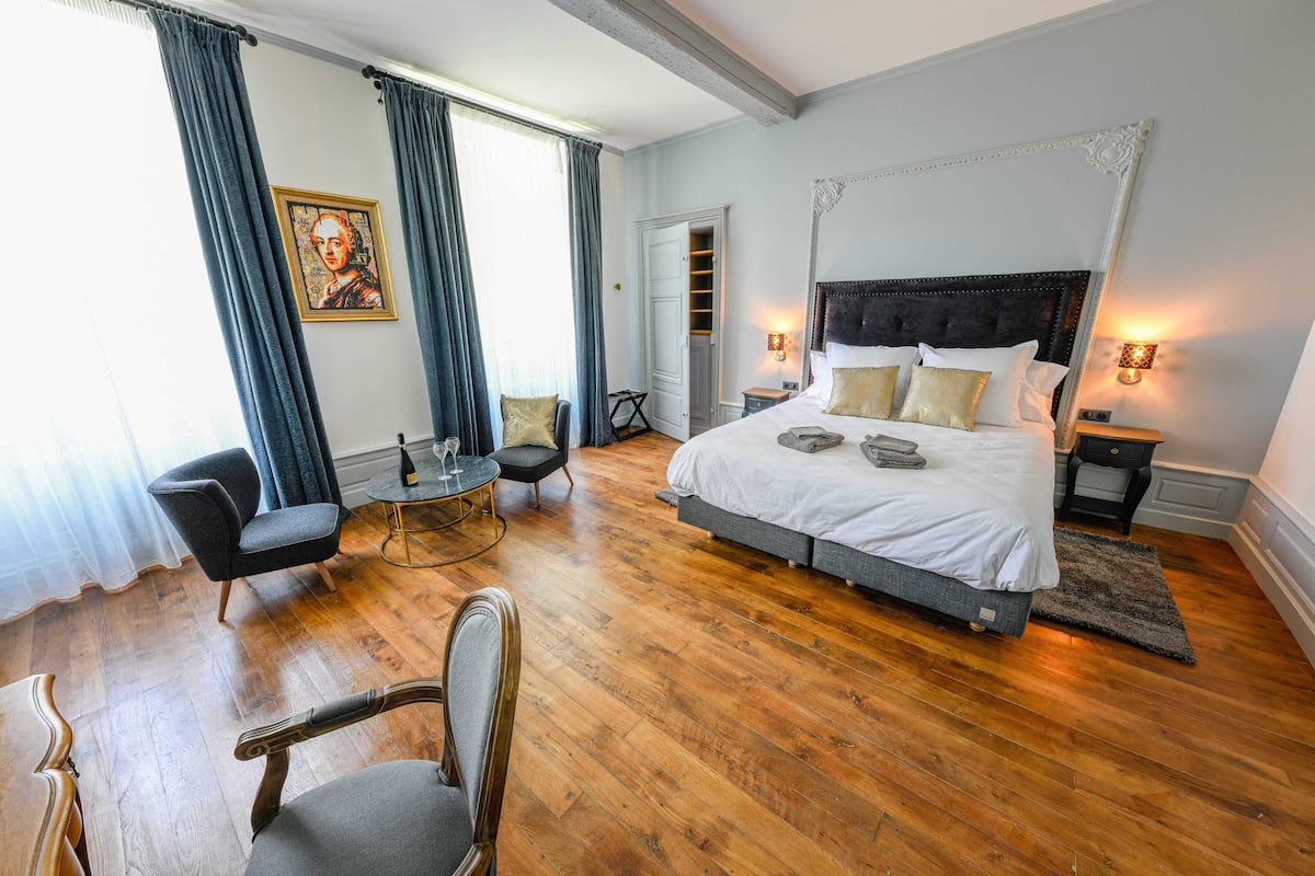 Une chambre spacieuse avec un grand lit, un coin salon avec une table et une armoire.