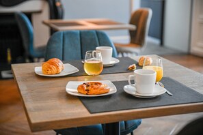 Een ontbijtje met croissants, een glas thee en een kop koffie op een houten tafel.