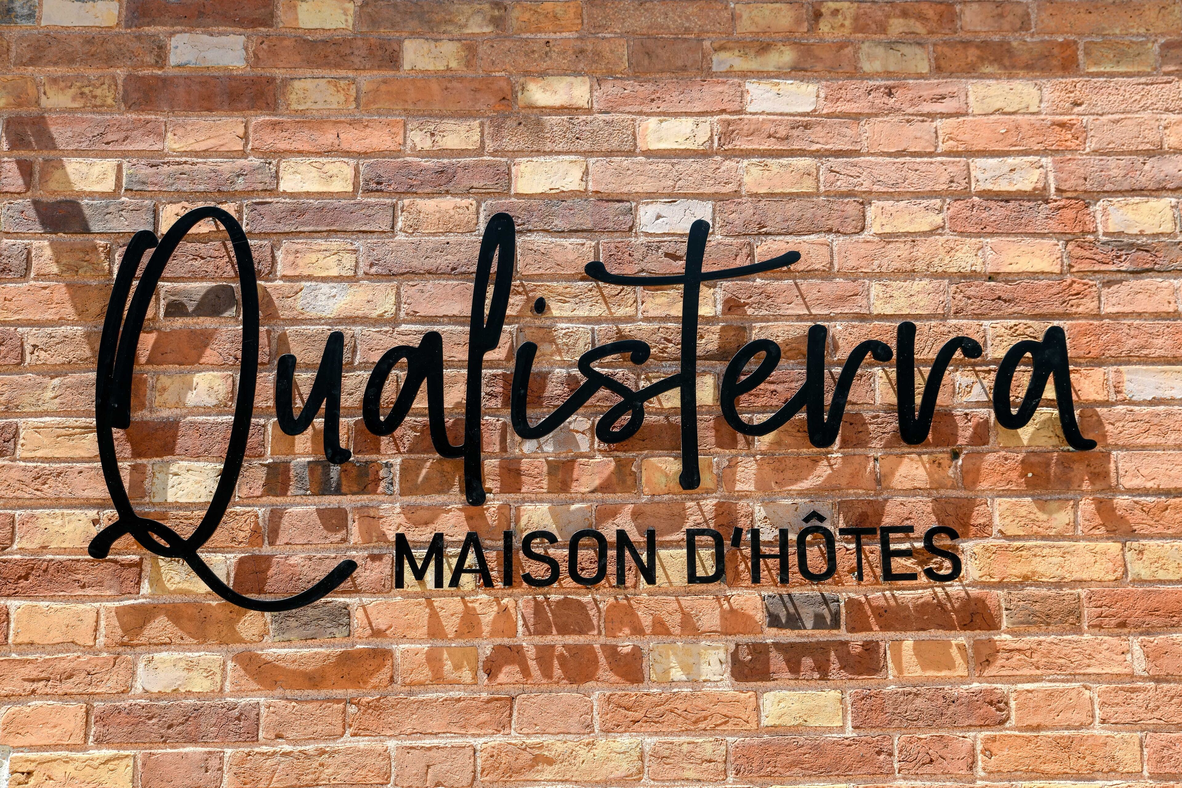 A brick wall with the text "Qualisterra MAISON D'HÔTES" in black.