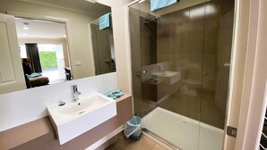 Un baño moderno con ducha de vidrio, lavamanos blanco y un espejo grande.