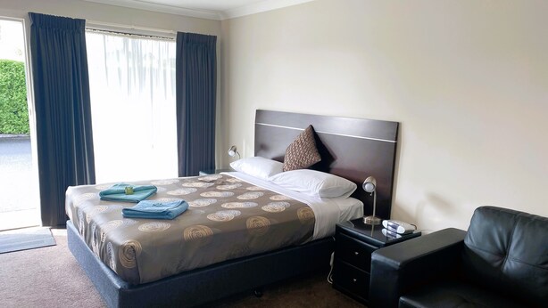 Habitación de hotel con cama, mesita de noche, lámpara, sofá de cuero negro y vista a zonas verdes.